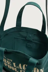 Bolso tipo shopper verde oscuro de tejido de algodón, con doble asa de mano y estampado frontal en color beige con la inscripción "The Lagoon Pool Club Palm Springs California".