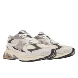 Championes urbanos New Balance modelo 2010, con diseño de paneles en tonos gris, beige y crema. Presentan una combinación de malla técnica y superposiciones de gamuza, con el logo N característico en el lateral y una entresuela robusta con detalles en color bronce.