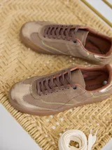 Championes de cuero color tostado con detalles metalizados y pespuntes decorativos en verde y azul. Cuentan con cordones marrones y suela de goma texturizada.