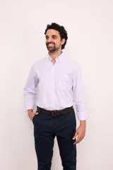 Camisa de corte clásico confeccionada en algodón, con diseño de rayas verticales finas en color rosa sobre fondo blanco. Presenta cuello abotonado, cierre frontal con botones, mangas largas con puños abotonados y un bolsillo en el pecho con el logo de la marca bordado.