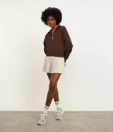Campera deportiva femenina color marrón, ligeramente cropped, con cuello alto y cierre frontal de cremallera invisible. Presenta mangas largas con detalles contrastantes en blanco, puños y bajo con acabado.