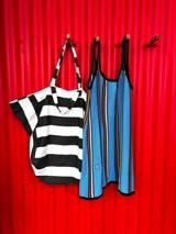 Vestido corto blanco con rayas verticales en azul, amarillo y marrón. Tiene escote redondo, breteles anchos y corte holgado.