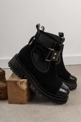 Bota tipo Chelsea de cuero marrón con suela track negra de goma. Presenta paneles elásticos laterales y una costura reforzada en la puntera. Incluye una correa de cuero desmontable con hebilla metálica.