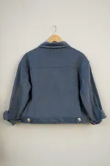 Campera azul de pana con cuello clásico, cierre frontal con botones dorados, bolsillos con solapa en el pecho y mangas largas con puños arremangados.