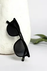 Lentes de sol negros con montura redonda y detalles geométricos en las esquinas superiores.