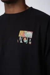 Remera de corte oversize color beige, confeccionada en algodón grueso. Presenta una estampa frontal pequeña con diseño artístico abstracto en tonos azules y amarillos.
