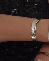 Pulsera tipo esclava abierta con diseño rústico y acabado irregular, fabricada en bronce y alpaca.