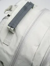 Mochila color arena con detalles en gris y negro. Cuenta con un compartimento principal con cierre, un bolsillo frontal con cordón elástico y bolsillos laterales de malla.