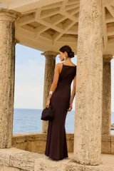 Vestido largo color chocolate con tirantes finos, escote recto y detalle de nudo en la cintura que crea una abertura en la falda.