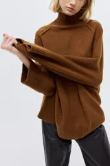 Buzo oversized de punto suave con cuello tortuga acanalado y abertura en la nuca. Presenta mangas raglán con costuras decorativas y terminaciones acanaladas en puños y bajo.
