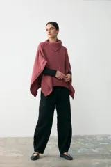 Capita de tejido de punto grueso en color rosa, con cuello alto y diseño holgado tipo poncho con aberturas laterales para los brazos.