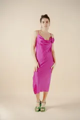Vestido midi fucsia de satén, con escote buche, breteles finos y detalle de rosa de tela aplicada en el escote. Presenta un tajo lateral en la falda y calce al cuerpo.