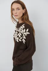 Buzo de tejido de punto en color beige, con cuello redondo y mangas largas. Presenta un delicado bordado de ramas y hojas en color crema en la parte superior del frente.