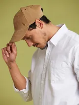 Gorro con visera color marrón claro, confeccionado en algodón con logo metálico de la marca en el frente.