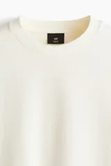 Remera de algodón en punto liviano color beige, con diseño boxy de hombros caídos, cuello redondo con ribete acanalado y corte oversized.