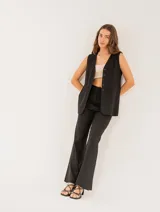 Pantalón negro de lino, tiro alto, corte palazo, con elástico en la pretina trasera, cierre delantero y broche interno. Tiene bolsillos laterales, dobladillo invisible y tajos a los costados.