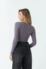 Top de manga larga en tejido rib negro, con escote en V profundo y detalle de nudo frontal que genera un efecto fruncido.