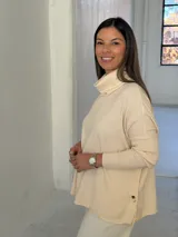 Polerón de punto color crudo con cuello alto tipo polera, mangas largas con puños acanalados y diseño holgado con aberturas laterales.