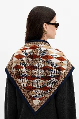 Pañuelo cuadrado de seda con estampado geométrico de rombos en tonos terracota, beige y azul marino, con borde oscuro y detalle de monograma en los extremos.