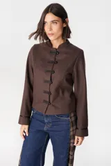 Chaqueta de paño color marrón, de silueta ajustada, con cuello mao y cierre frontal con presillas y botones redondos. Presenta detalles de cintas en los puños.