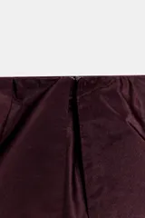 Falda midi asimétrica de color bordó, confeccionada en tejido satinado con volumen. Presenta un diseño con volados en la cintura y cierre de cremallera oculta en la espalda.