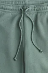 Pantalón de jogging verde con interior cepillado suave, cintura elástica fruncida con cordón ajustable, bolsillos laterales discretos y elástico revestido en los bajos.