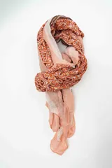 Pañuelo rectangular de tejido fino con estampado geométrico y tribal en tonos naranja, terracota y rosa pálido, con bordes en rayas verticales.