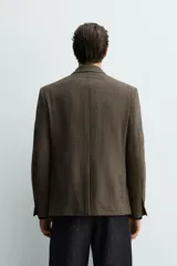 Blazer de corte relajado confeccionada en tejido con lana, con diseño de cuadros pequeños. Presenta cuello con solapas de pico, cierre frontal de botonadura cruzada, manga larga con botones en los puños y bolsillos de vivo en el pecho y la cadera.