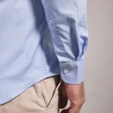 Camisa de vestir celeste a rayas verticales blancas, de corte clásico, con cuello abotonado y manga larga.