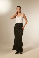 Falda larga negra de corte tubo, cubierta completamente de lentejuelas brillantes. Presenta una abertura lateral en la pierna.