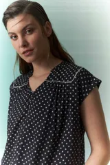 Blusa negra con lunares blancos, escote en V y cuello bebé con borde blanco.