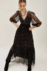 Vestido midi de tul negro con bordados brillantes y pedrería en el escote. Presenta mangas abullonadas, corte imperio y falda con volado en el ruedo. Incluye viso interior.