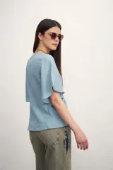 Camisa negra con botones dorados, escote en V y mangas cortas amplias con lazos laterales. 