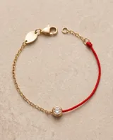 Pulsera de hilo rojo de seda combinada con cadena de acero con baño de oro, con un dije redondo central tipo punto de luz engastado con circorias.