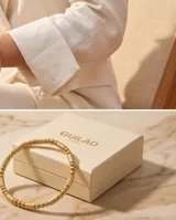 Pulsera tipo esclava rígida de acero con baño de oro, con diseño de eslabones texturizados y esferas lisas intercaladas.