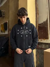 Canguro negro con cierre frontal, capucha y bolsillos tipo canguro. Presenta un estampado frontal en color blanco con un diseño ovalado rodeado de estrellas.