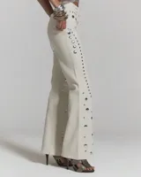 Jeans de corte recto color crudo con apliques de tachas metálicas plateadas distribuidas en patrones geométricos.