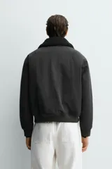 Cazadora bomber de corte cropped confeccionada en algodón, color negro. Presenta cuello de solapa con efecto borreguillo a contraste, cierre frontal con cremallera metálica, bolsillos delanteros tipo plastrón con solapa y acabados en rib en puños y bajo.