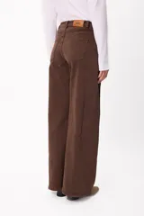 Jean de corte wide leg en color marrón chocolate, con tiro medio y cierre frontal con botón y cremallera. Presenta un diseño de cinco bolsillos y costuras visibles.