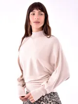 Buzo de punto color beige claro, con cuello alto, mangas largas tipo murciélago y puños ajustados. El bajo del buzo es ajustado y cruzado.