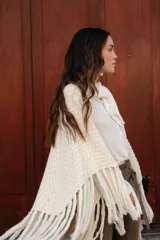Poncho triangular de lana en color crudo, con diseño de tejido texturizado y terminaciones de flecos largos en todo el borde.