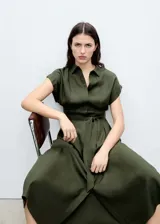 Vestido midi de corte evasé en color verde oliva, con cuello camisero, cierre frontal de botones y mangas cortas con dobladillo. Incluye un cinturón de la misma tela para ajustar a la cintura y detalle de pinzas delanteras.
