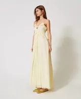 Vestido largo color amarillo pálido, confeccionado en georgette con rayas de raso. Cuenta con tirantes finos, escote de pico decorado con volantes y falda fruncida de corte redondeado en la cintura. Prenda forrada, de corte holgado.