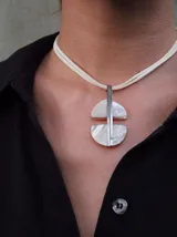 Collar con colgante geométrico de nácar y metal plateado, con cordón doble de gamuza color crema.