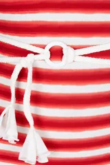 Traje de baño entero de una sola pieza con diseño asimétrico de un solo hombro. Presenta un estampado de rayas horizontales rojas y blancas, y un cinturón blanco de cuerda con borlas y un aro central.