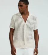 Camisa de manga corta color beige, con cuello solapa, cierre frontal de botones y textura tejida a rayas verticales. Marca Marfinno.