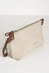 Sobre de mano tipo clutch confeccionado en cuero agamuzado color beige, con cierre metálico superior, detalles en cuero marrón en los extremos y correa de muñeca desmontable. Presenta el logo de la marca grabado en el frente.