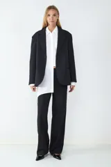 Pantalón negro de tiro medio con pliegues frontales, confeccionado en tejido sastrero fluido. Presenta piernas amplias, bolsillos laterales y cierre frontal con cremallera y botón.