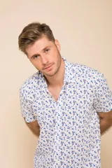 Camisa de manga corta con cierre frontal de botones y cuello clásico. Presenta un estampado floral en tonos azules sobre fondo blanco.