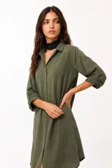 Vestido camisero de color marrón oscuro, con cuello clásico, cierre frontal de botones y mangas largas. Presenta un corte midi con caída fluida.